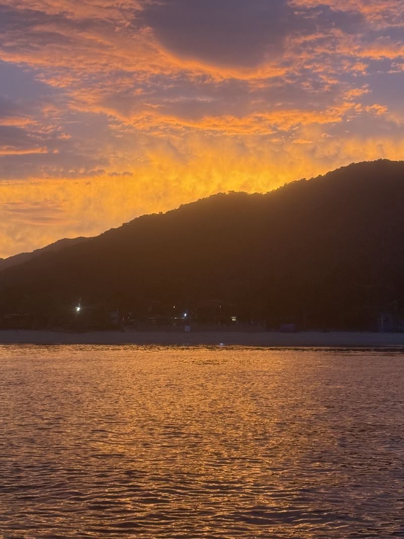 Pôr do sol alaranjado sobre a baía e o morro