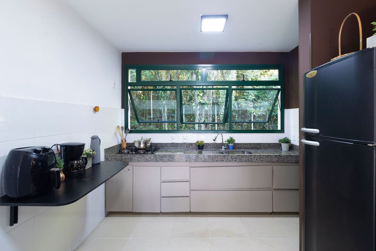 Cozinha com geladeira e janela para a mata