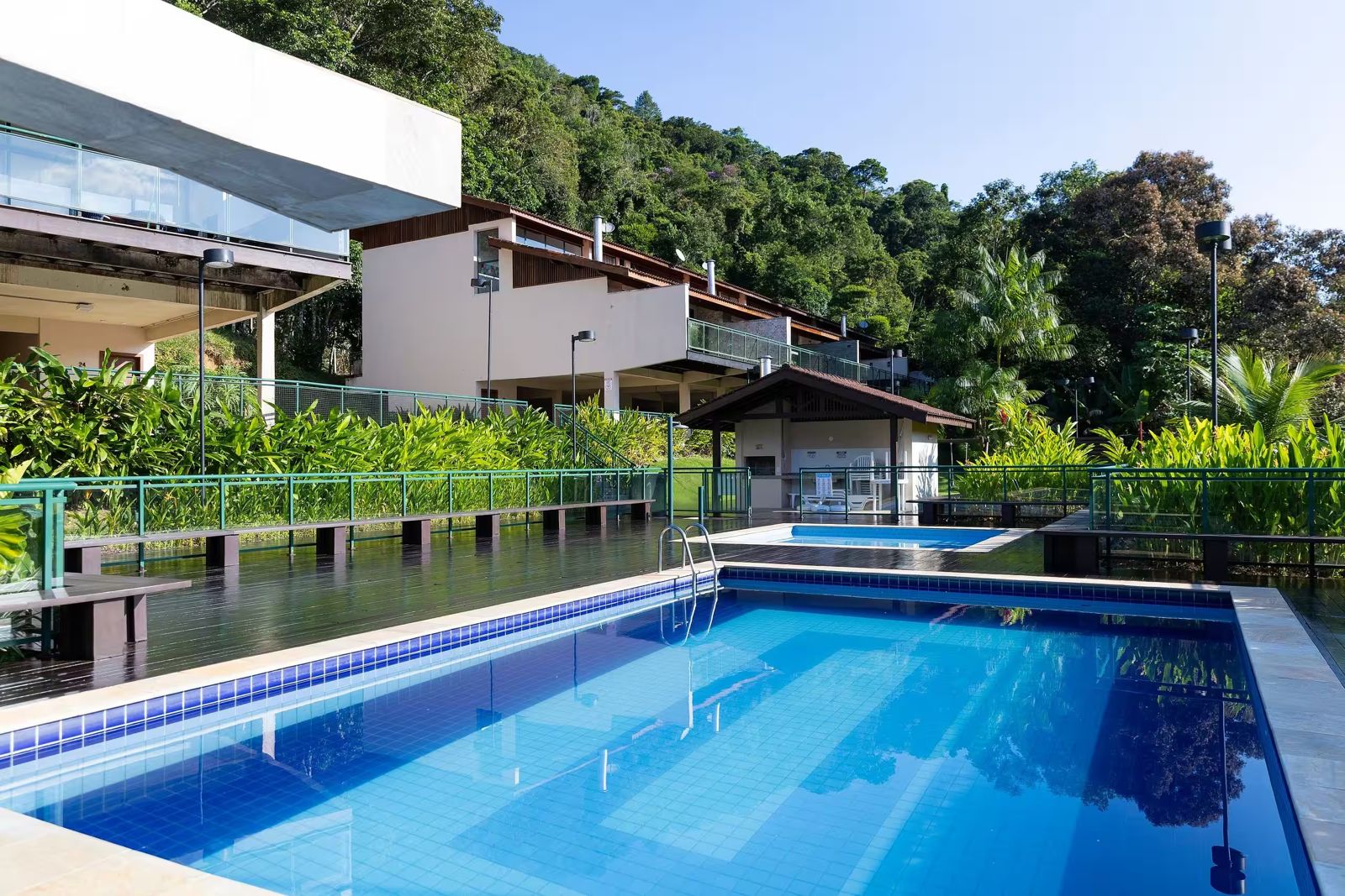 Piscina do condomínio com deck e a mata ao fundo