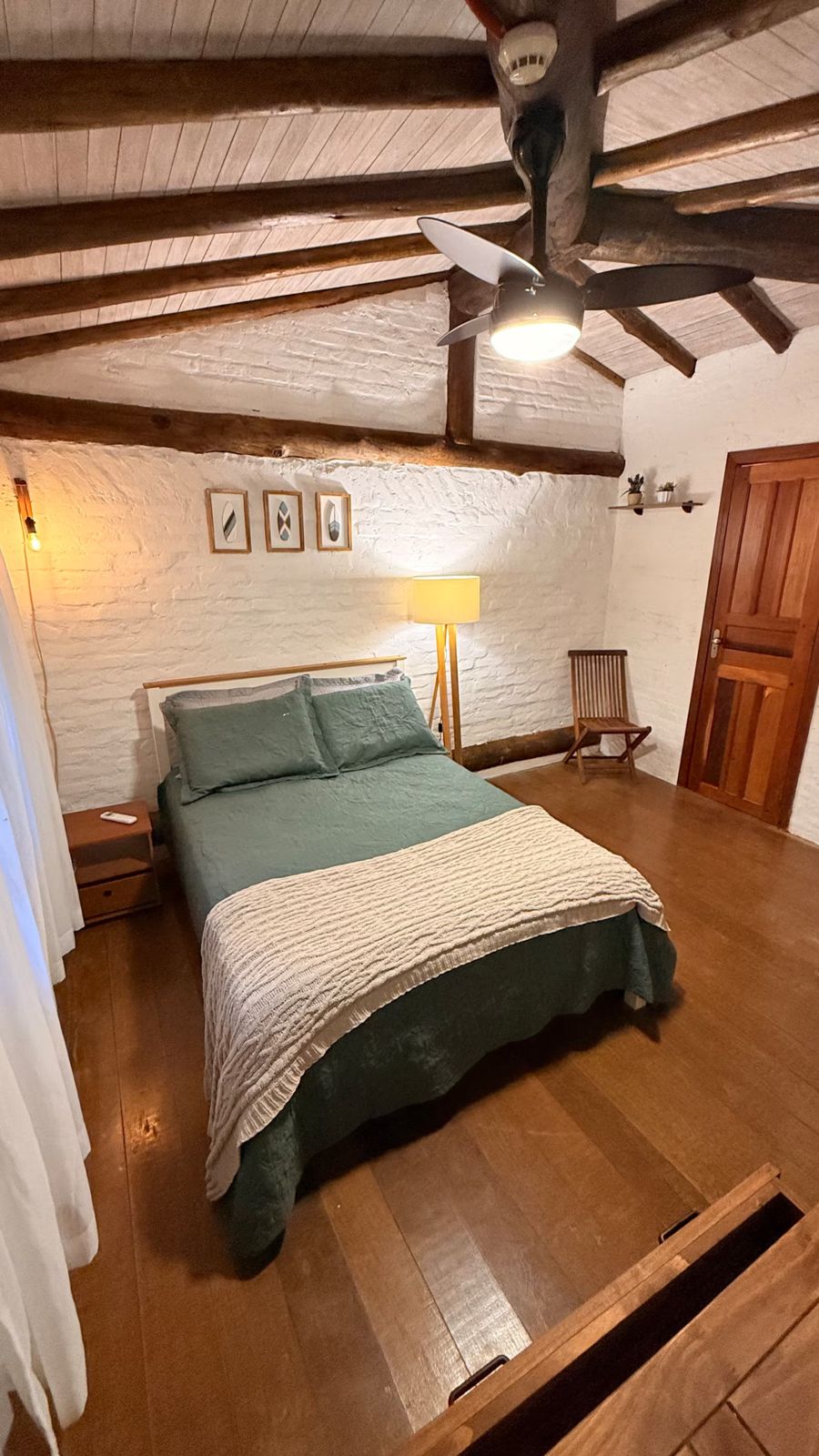 Suíte com cama de casal, piso de madeira e vigas aparentes