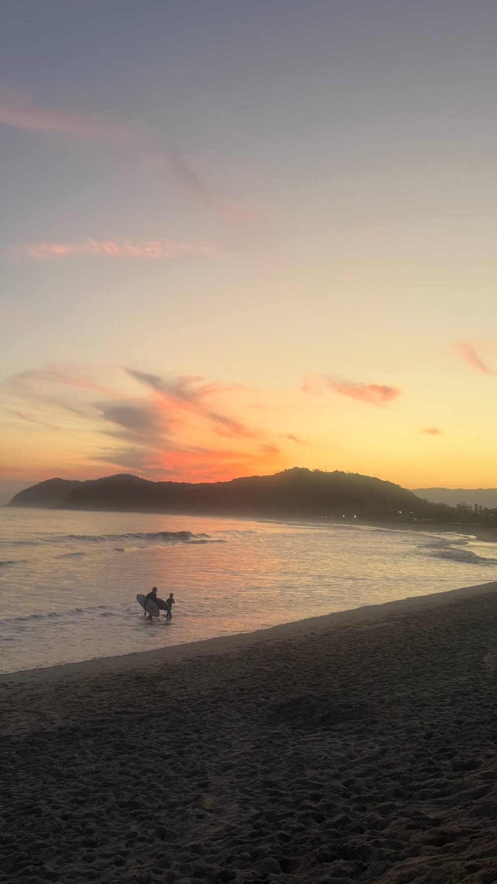 Pai e filho saindo do mar com pranchas no fim de tarde