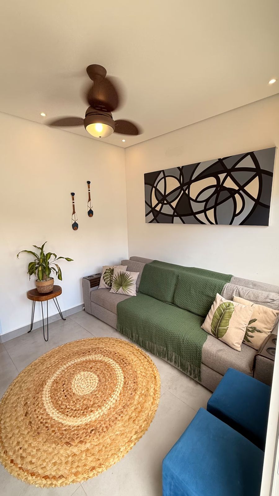 Sala com sofá verde, tapete redondo e ventilador de teto
