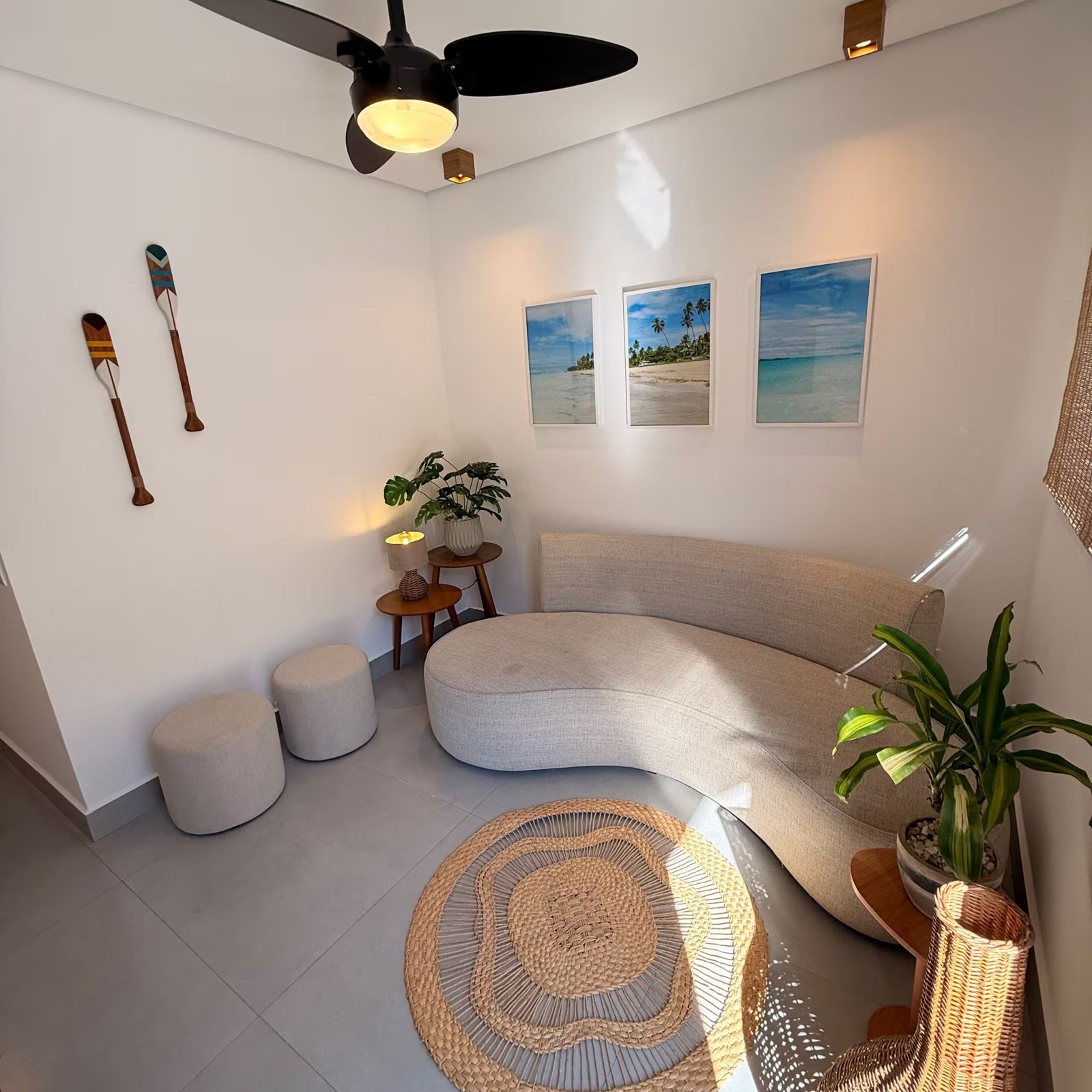Sala com sofá curvo, tapete redondo e quadros de praia