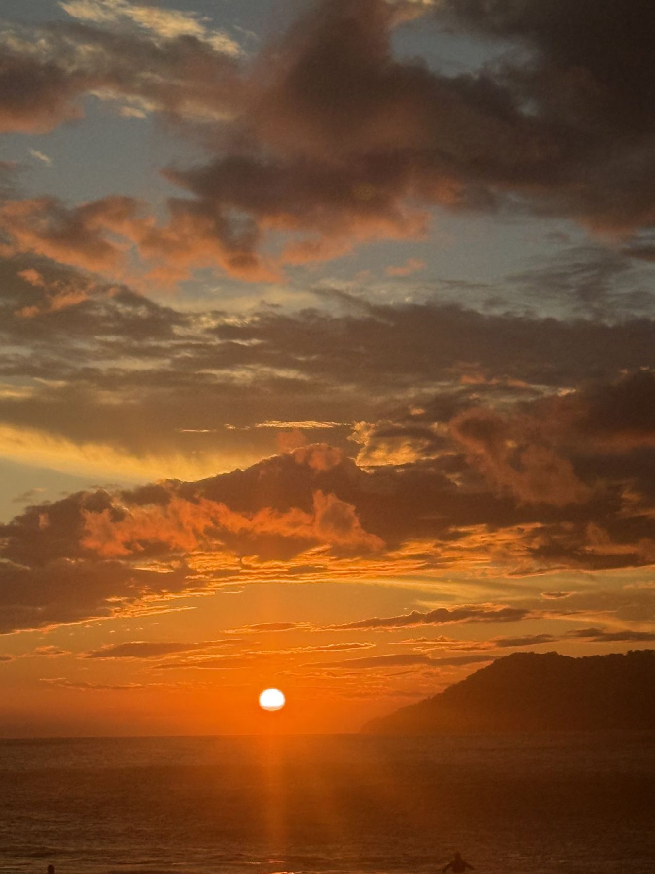 Pôr do sol sobre o mar, com o morro à direita